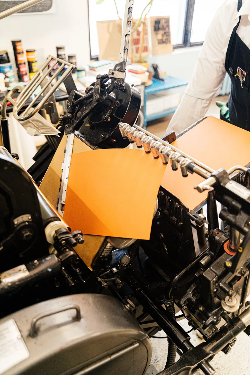Orange paper passing through a traditional printing press